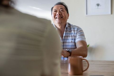 Senior Asian Man Smiling with Coffee Mug at Dining Table