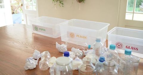 Home recycling station showing clear bins labeled paper plastic glass on wooden table