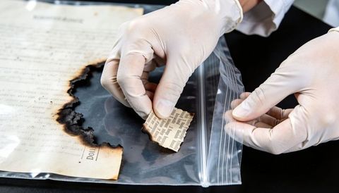Conservator handling charred archival document fragments with gloves and resealable bag