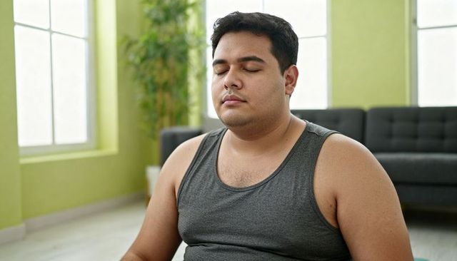 Calm young man meditating at home in gray tank top, natural light living room, mindfulness