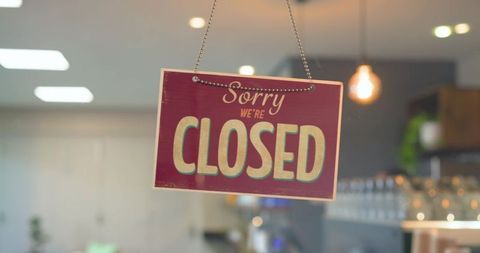 Retro maroon closed sign hanging on glass door with warm pendant bulb and cafe bokeh