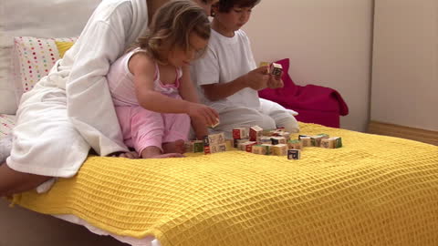 Mother and Children Playing with Blocks on Cozy Bed