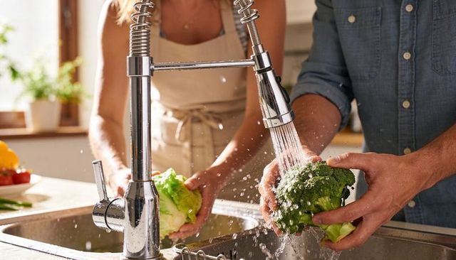 Couple rinsing fresh lettuce and broccoli at sunlit kitchen sink
