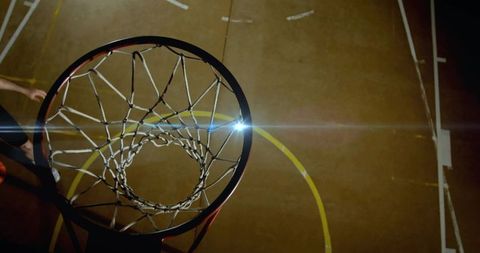 Overhead basketball hoop and braided net framing indoor court with lens flare and motion
