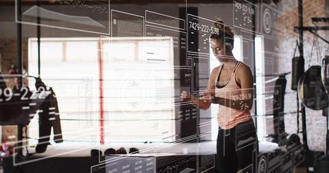 Female athlete checking fitness app in industrial gym with augmented reality data overlay