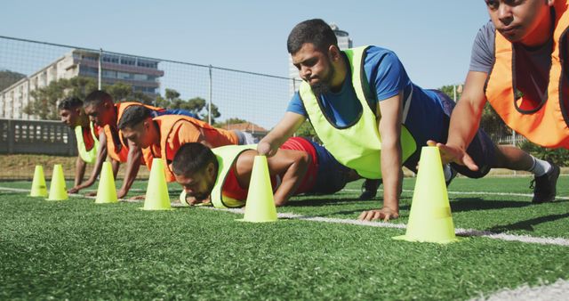 Diverse male football players training and doing push-ups on outdoor pitch. Football, sports and teamwork.