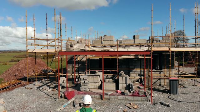 Engineer in a hard hat supervising a building under construction against a blue sky with white clouds. Ideal for construction, engineering, project management, and real estate development themes. Perfect for illustrating concepts of supervision, safety, and progress in the building industry.