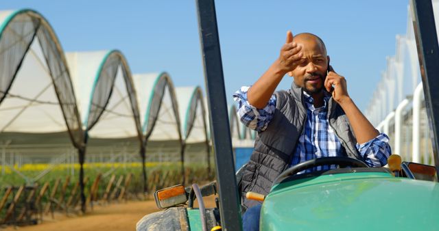 Farmer discussing work over phone while driving tractor near greenhouses - Download Free Stock Images Pikwizard.com