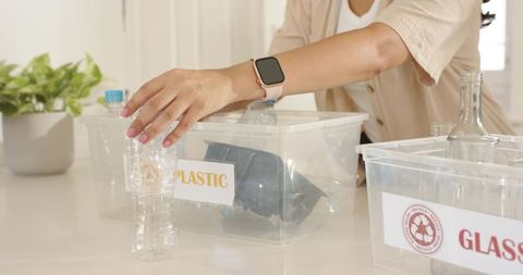 Woman sorting recycling at kitchen counter placing plastic bottle into labeled bin