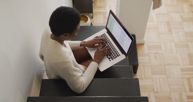Happy african american woman sitting on stairs, using laptop. domestic life, spending time at home.