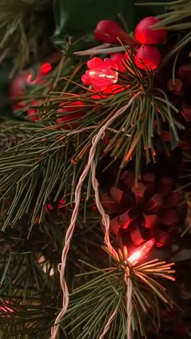 Vertical close-up revealing pine cluster with pinecone, red berries and glowing LED lights