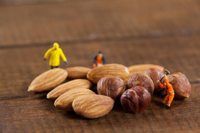 Miniature workers are depicted working with almonds and nuts on a wooden surface, creating a playful and creative scene. This image can be used for concepts related to food, creativity, teamwork, and construction. It is ideal for advertising, blogs, and social media posts that aim to capture attention with unique and imaginative visuals.