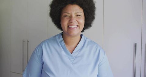 Smiling female healthcare professional in light blue scrubs standing in modern clinic