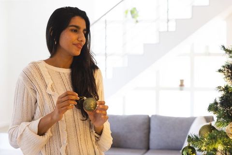Woman Decorating Christmas Tree Indoors with Green Ornament