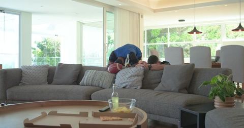 Friends leaning over sofa cheering with football and drinks during game day