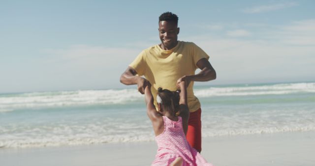 Father and daughter playing on sandy beach near ocean. Father spins daughter while she laughs. Ideal for concepts of family bonding, joy, outdoor activities, summer vacations, and parental love.