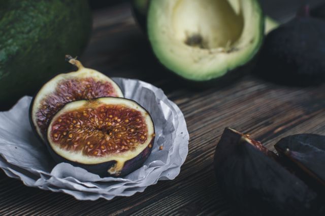 Close-up view of fresh ripe figs cut in half and whole avocado on wooden table. Ideal for use in food blogs, websites about healthy eating, organic lifestyle, recipe articles, or print materials showcasing fresh produce.