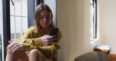 Woman Relaxing by Window Using Smartphone During Quarantine