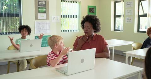 African American Teacher Guiding Student in Speech Practice with Laptops in Classroom