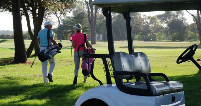 Couple walking on golf course carrying golf bags on a sunny day. Ideal for depicting leisure sports activities, outdoor fitness, and nature enjoyment. Perfect for use in golf lifestyle promotions, fitness campaigns, and outdoor activity advertisements.