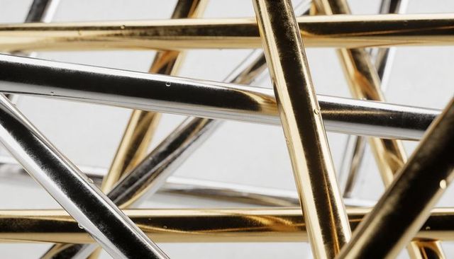 Interlaced gold and silver rods reflecting light with dew droplets and surface scratches
