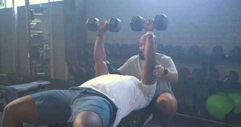 Personal Trainer Spotting Client Performing Dumbbell Bench Press on Flat Bench in Gym