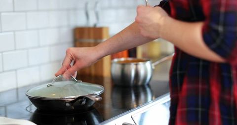 Person cooking in modern kitchen lifting pan lid