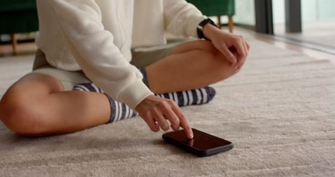 Woman Relaxing at Home Touching Smartphone on Carpeted Floor