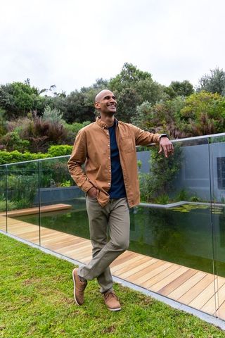 Asian man leaning on glass balustrade by modern pond, smiling, casual outdoor lifestyle