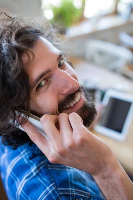 Portrait of smiling man looking back while talking on the mobile phone in coffee shop