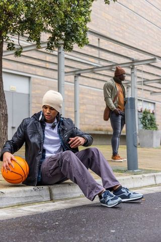 Urban friends sitting and standing with basketball in casual streetwear and beanies