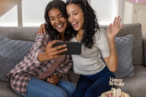 Mother and teenage daughter taking selfie on sofa during birthday celebration