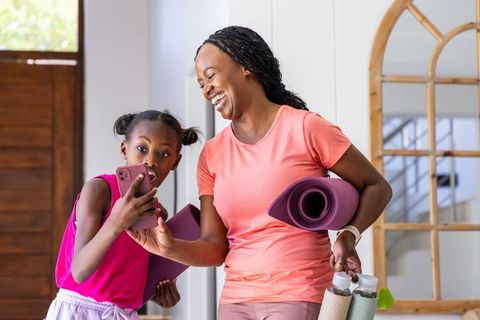 African american mother and daughter laughing together holding yoga mats and water bottles