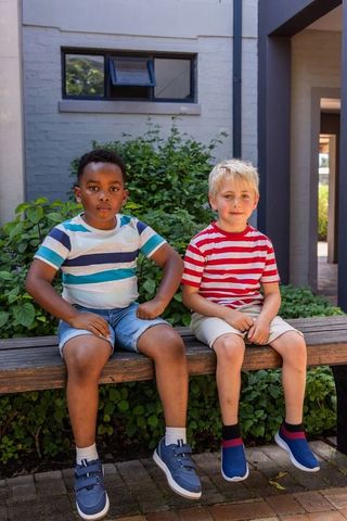 Black and white boys sitting on bench wearing striped tees and sneakers in courtyard