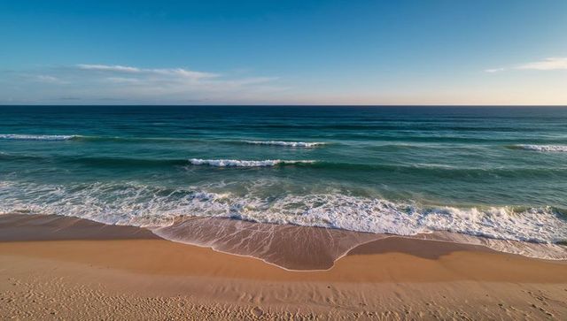 Rolling waves meeting golden sandy shoreline with soft seafoam and early morning light