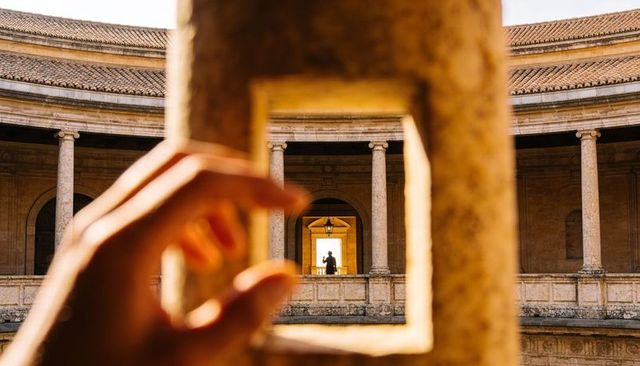 Hand framing square stone aperture in classical rotunda revealing silhouetted figure
