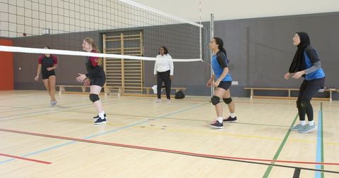 Female volleyball team practicing drills in school gym coach guiding players