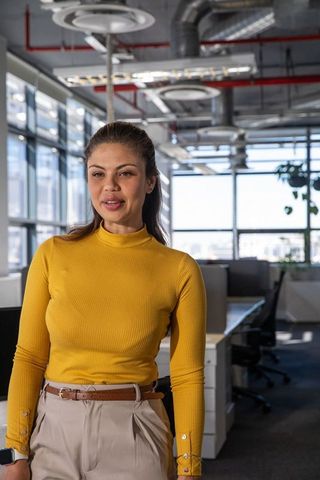 Professional woman speaking in modern open office wearing mustard top and beige trousers