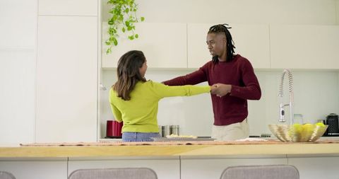 African American Man and Indian Woman Holding Hands and Dancing in Bright Modern Kitchen
