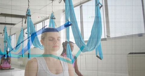 Women Meditating in Yoga Studio with Aerial Hammocks and Digital Overlay