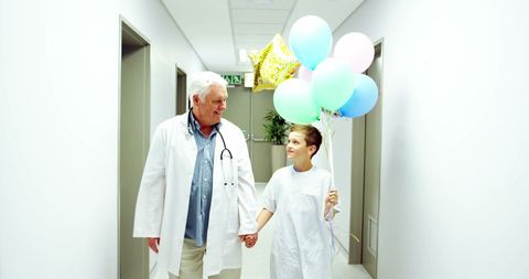 Senior Doctor with Girl Holding Balloons in Hospital Corridor