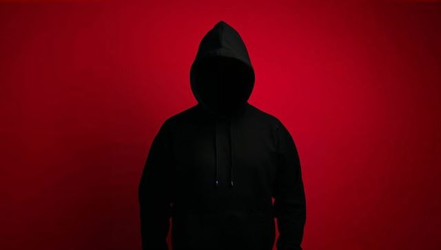 Silhouetted figure in hooded sweatshirt against red background