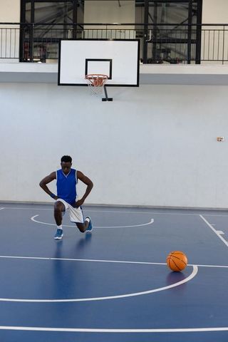 Basketball Player Kneeling to Stretch on Indoor Court Prepared for Training