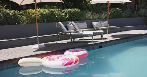 Colorful inflatable floats floating in backyard pool with lounge chairs and umbrellas
