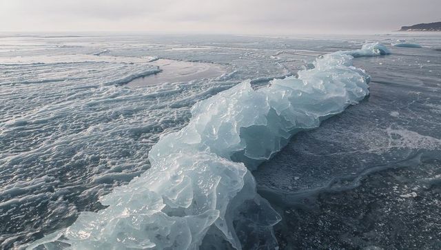 Translucent glass ice ridge cutting diagonally across frozen sea with distant headland