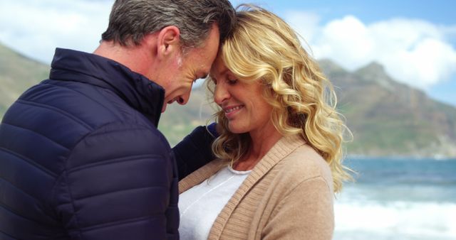 A middle-aged Caucasian couple shares an intimate moment by the sea, with copy space. Their affectionate embrace and serene backdrop suggest a romantic connection or a peaceful getaway.