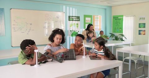 Diverse students exploring solar panel and tabletop wind turbine in bright stem classroom