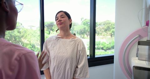 Asian woman receiving mammogram consultation from African-American nurse in sunlit clinic
