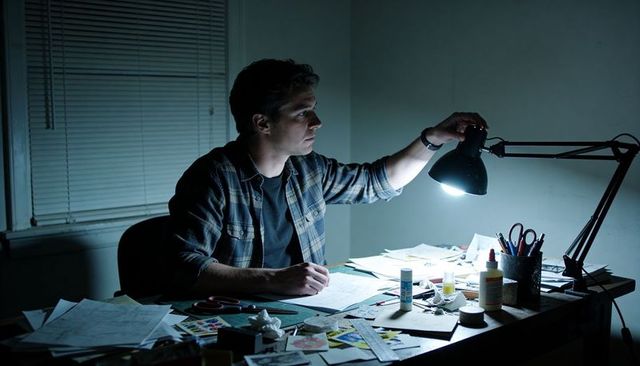 Man adjusting desk lamp while working late on sketches and crafts at cluttered worktable