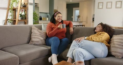 Friends relaxing on cozy grey sectional sofa sharing coffee and laughter in living room